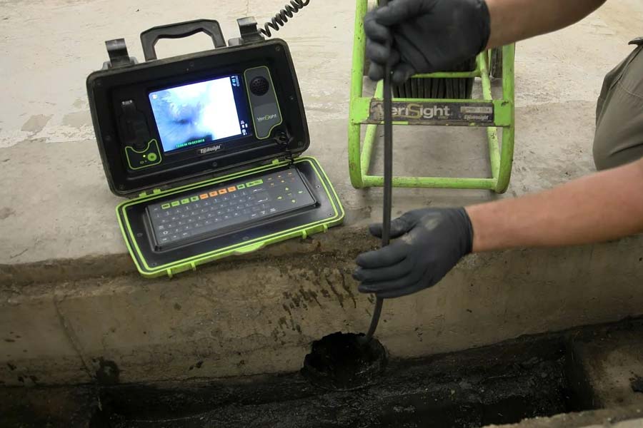 Hands inserting a video inspection camera into a drain pipe with a monitor showing the interior of the drain pipe.
